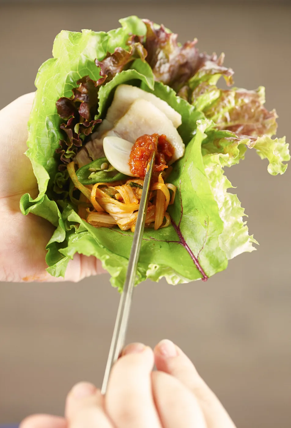 A lettuce wrap with grilled meat, ssamjang, garlic and rice beside banchan