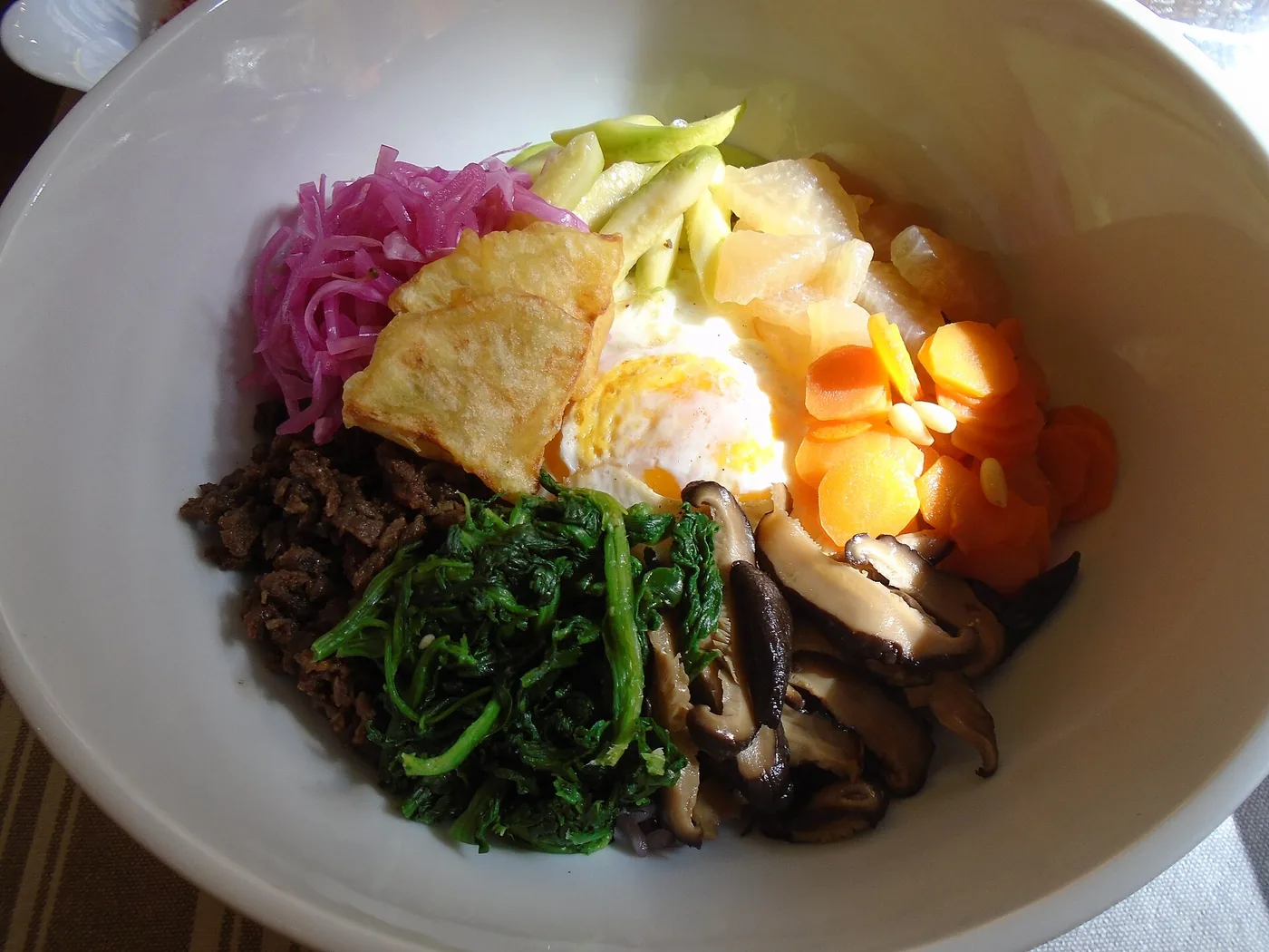 A bowl of bibimbap topped with vegetables, beef and egg