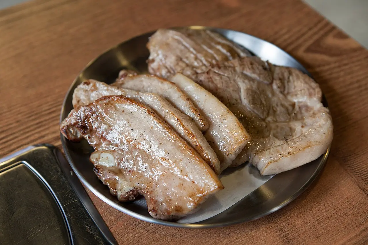 Thick slices of samgyeopsal pork belly cooking on a tabletop grill