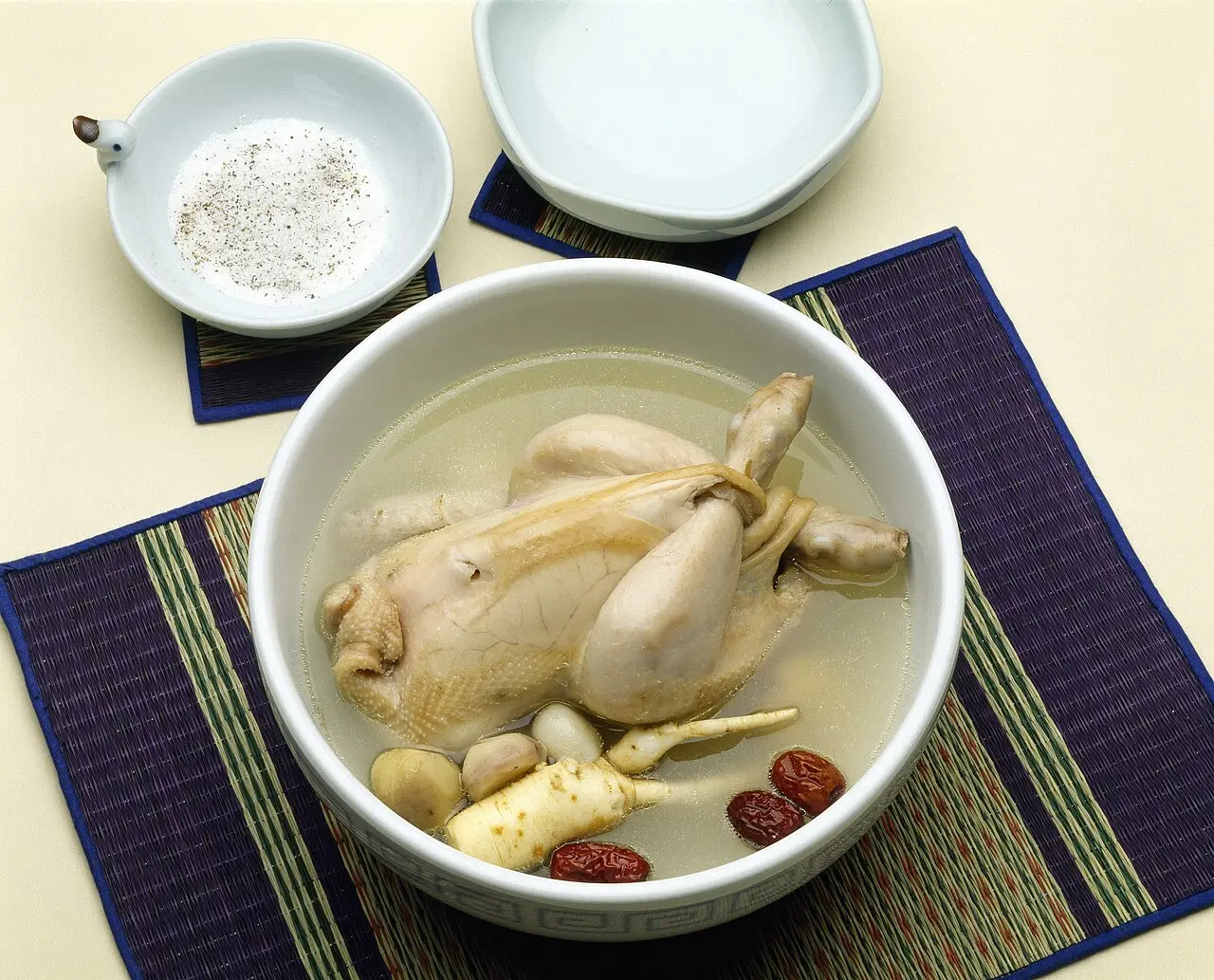 A whole young chicken in a bowl of samgyetang broth